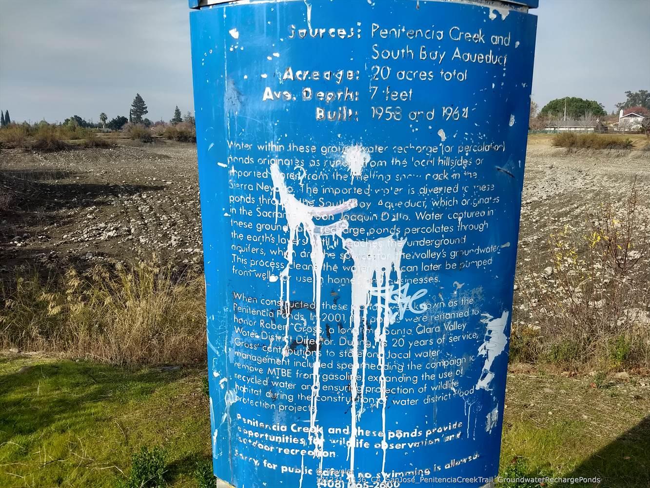 Blue informational sign covered in white paint, standing in a dry field.