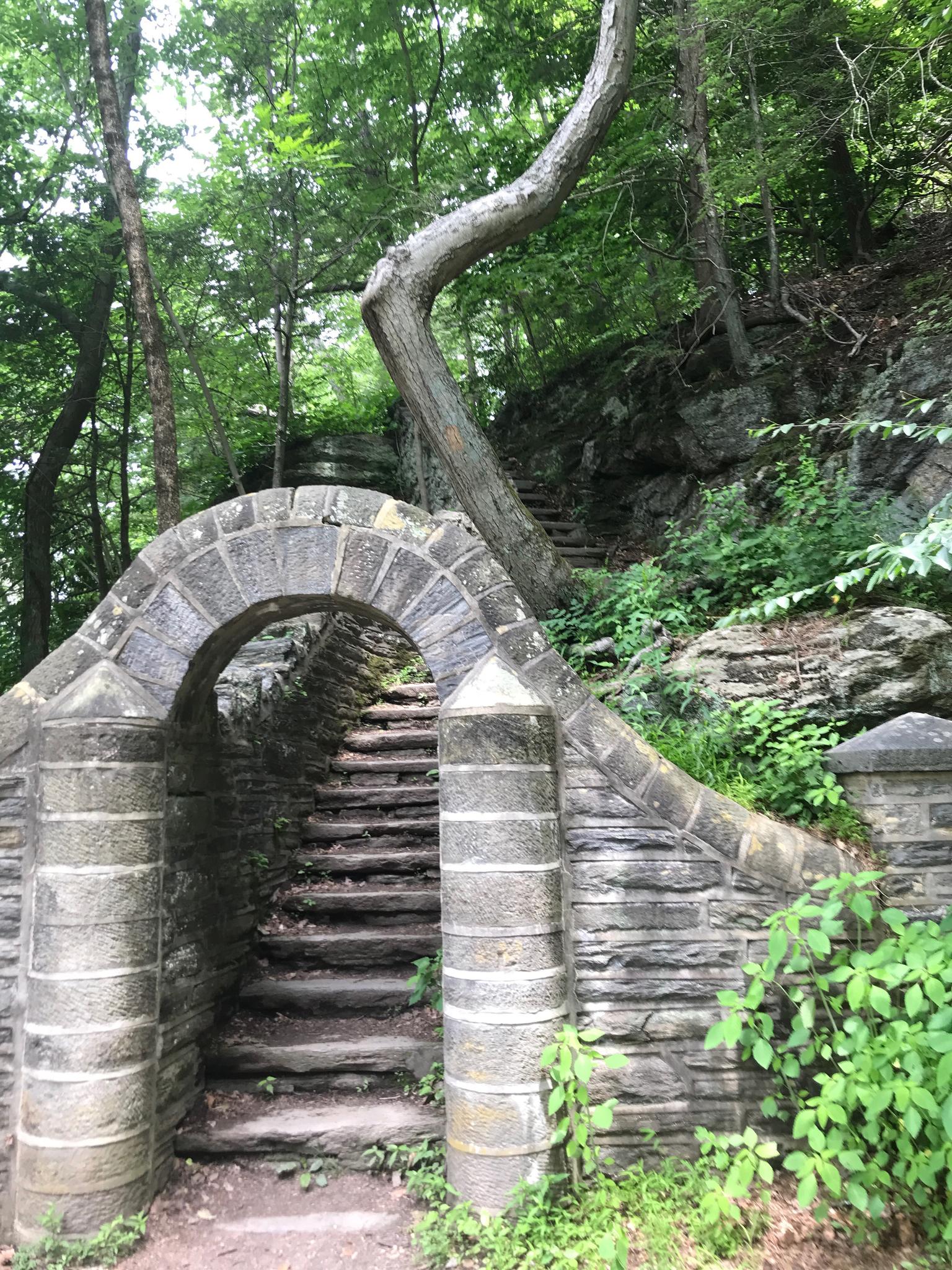 Stone archway and stairs ascend a rocky, tree-covered hillside.