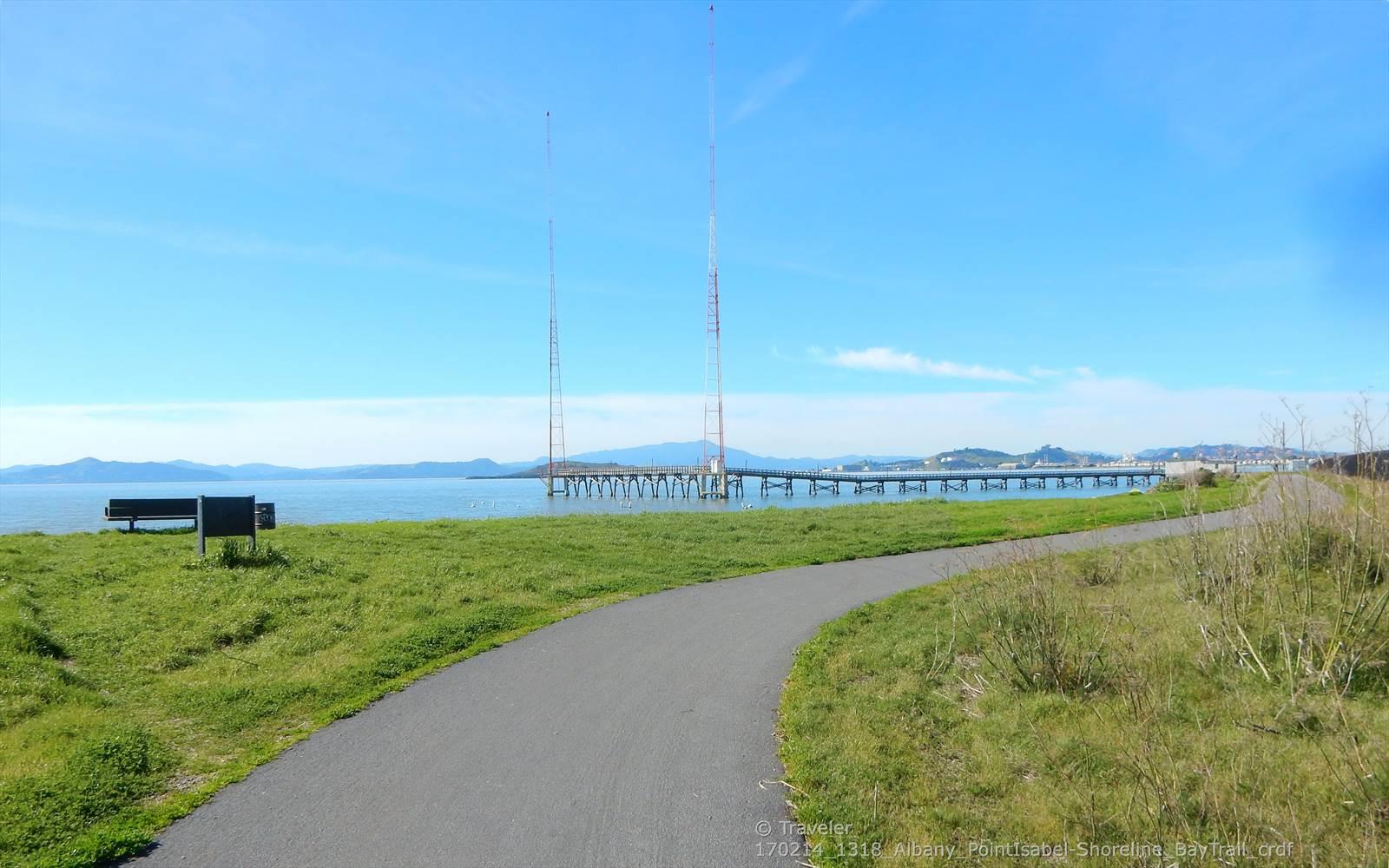 Paved path leading to a grassy area with benches overlooking a bay.