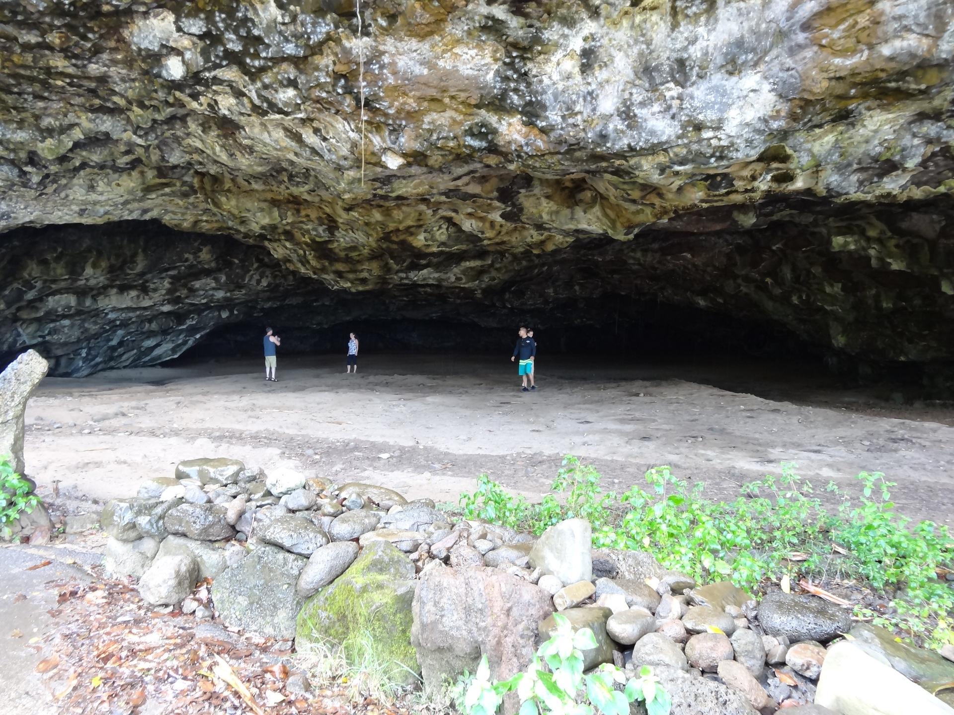 Three people exploring a vast, dimly lit cave with rocky ceiling and sandy floor.