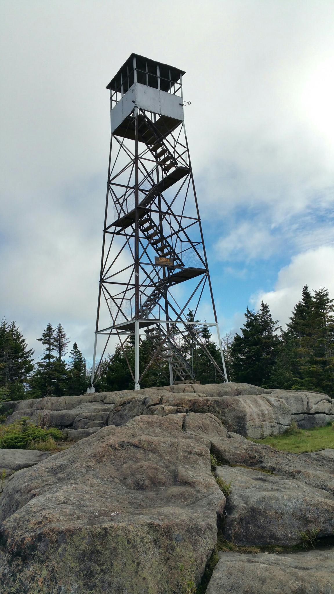 A tall metal fire lookout tower stands on a rocky summit.