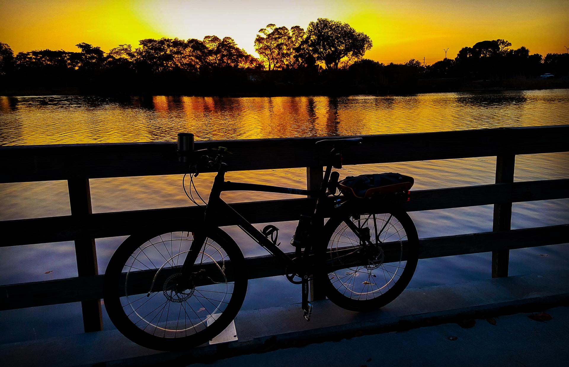 Bicycle silhouetted against a vibrant orange sunset over water and trees.