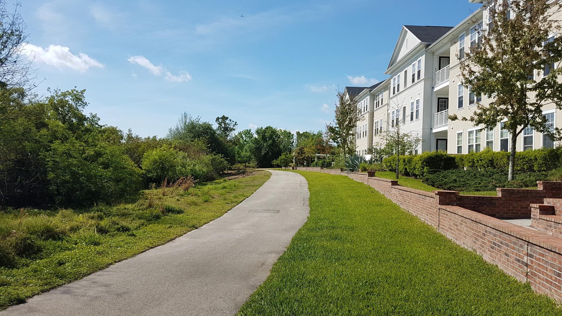 Paved path alongside a large building with green grass and trees.