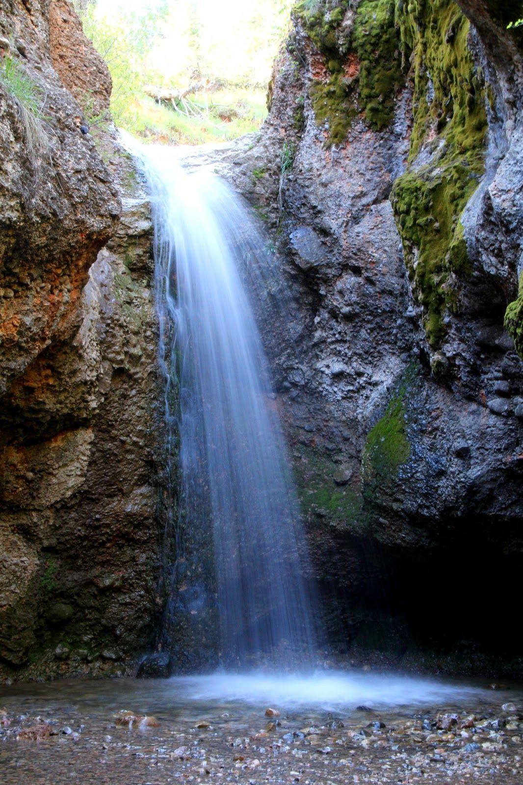 A waterfall cascades into a rocky pool within a mossy canyon, natural light.