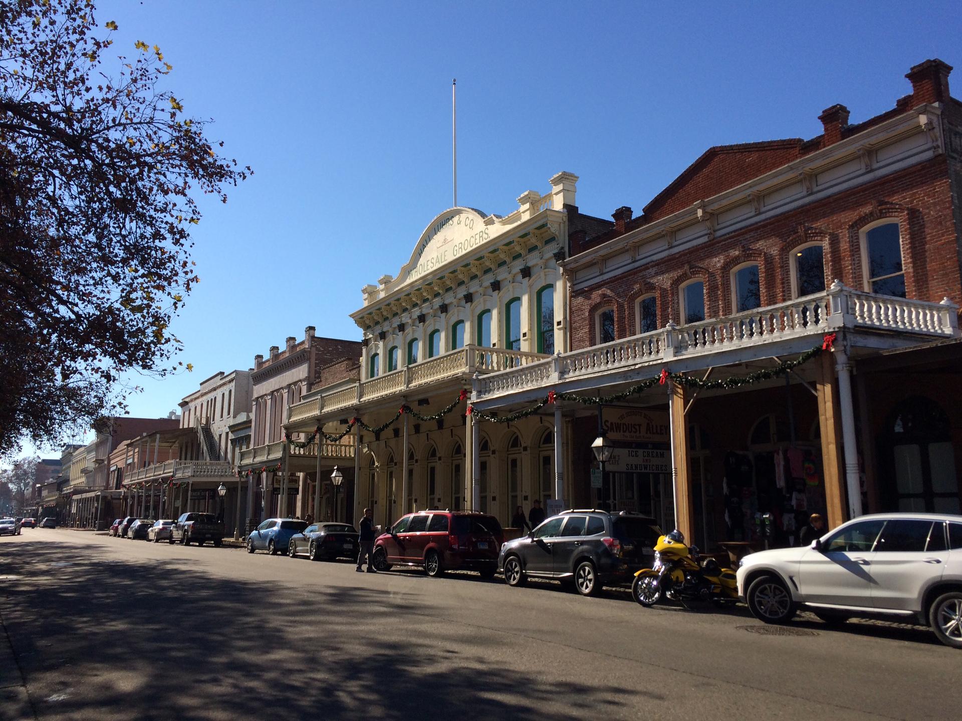 Historic street with ornate buildings, parked cars, and clear blue sky.