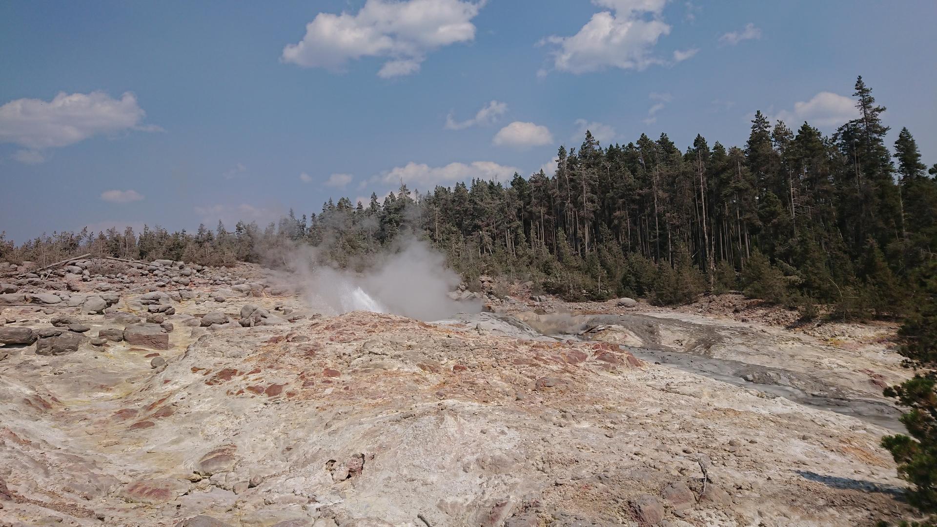 Steam rising from a fumarole in a rocky, colorful geothermal landscape.