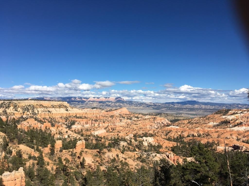 Expansive red rock landscape under a bright blue sky with scattered clouds.