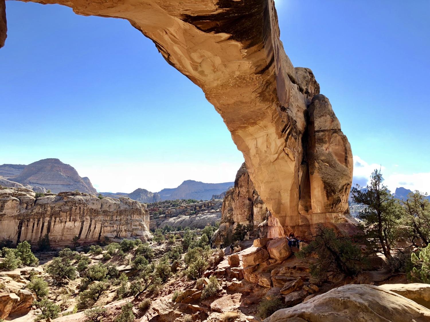 Massive natural rock arch framing a sunny desert valley with distant mountains.