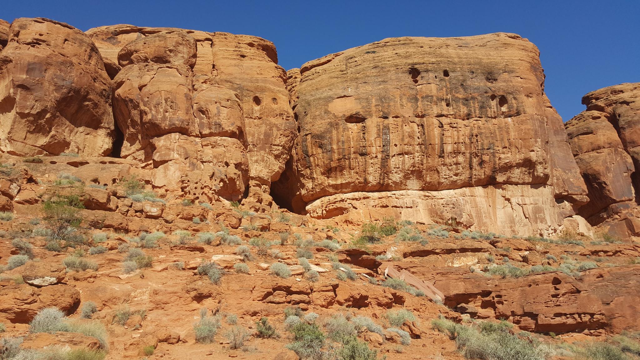Massive red rock formations with textured surfaces and small caves under a clear sky.