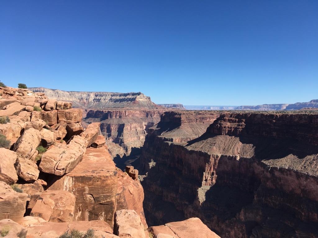 Vast, sunlit canyon with deep shadows and rugged rock formations under clear sky.
