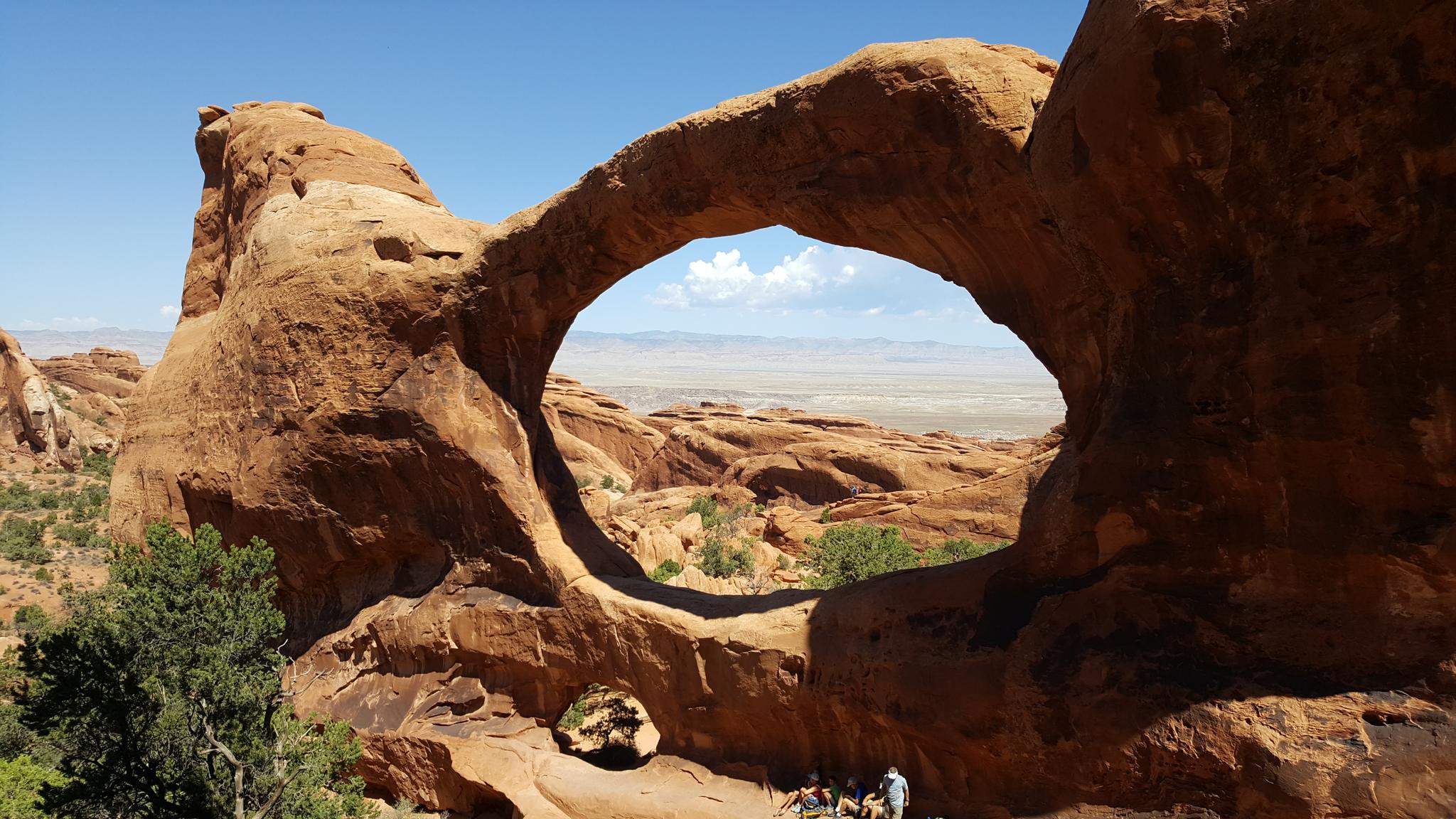 A large natural rock arch frames a distant desert landscape.