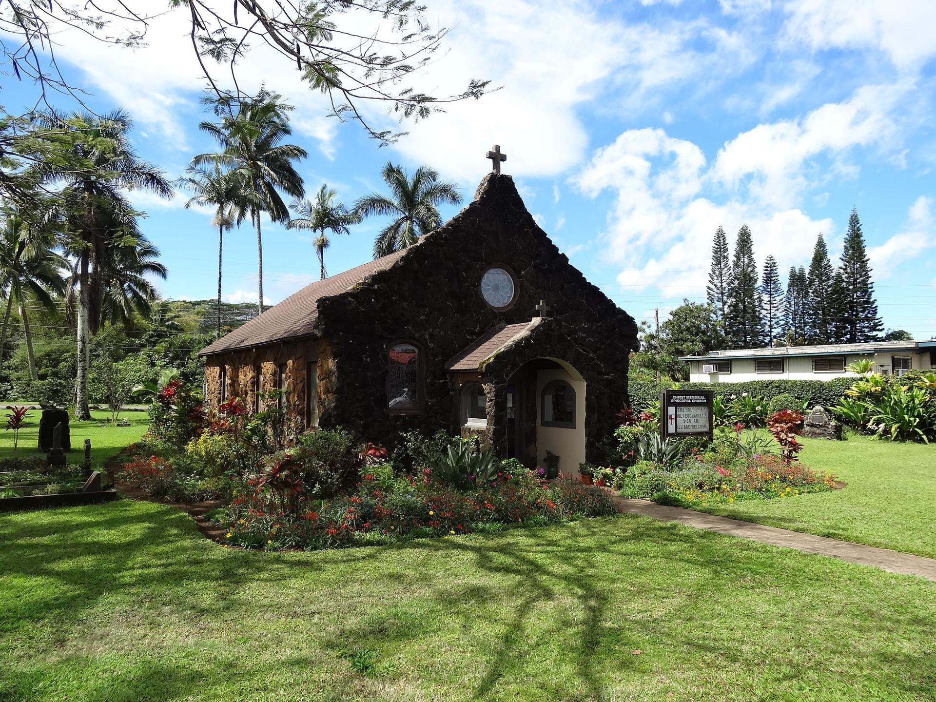 Historic stone church in a vibrant garden with palm trees on a sunny day.