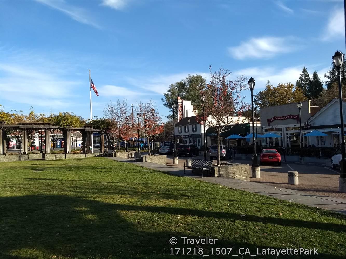 Sunny town square with green grass, buildings, and an American flag flying.