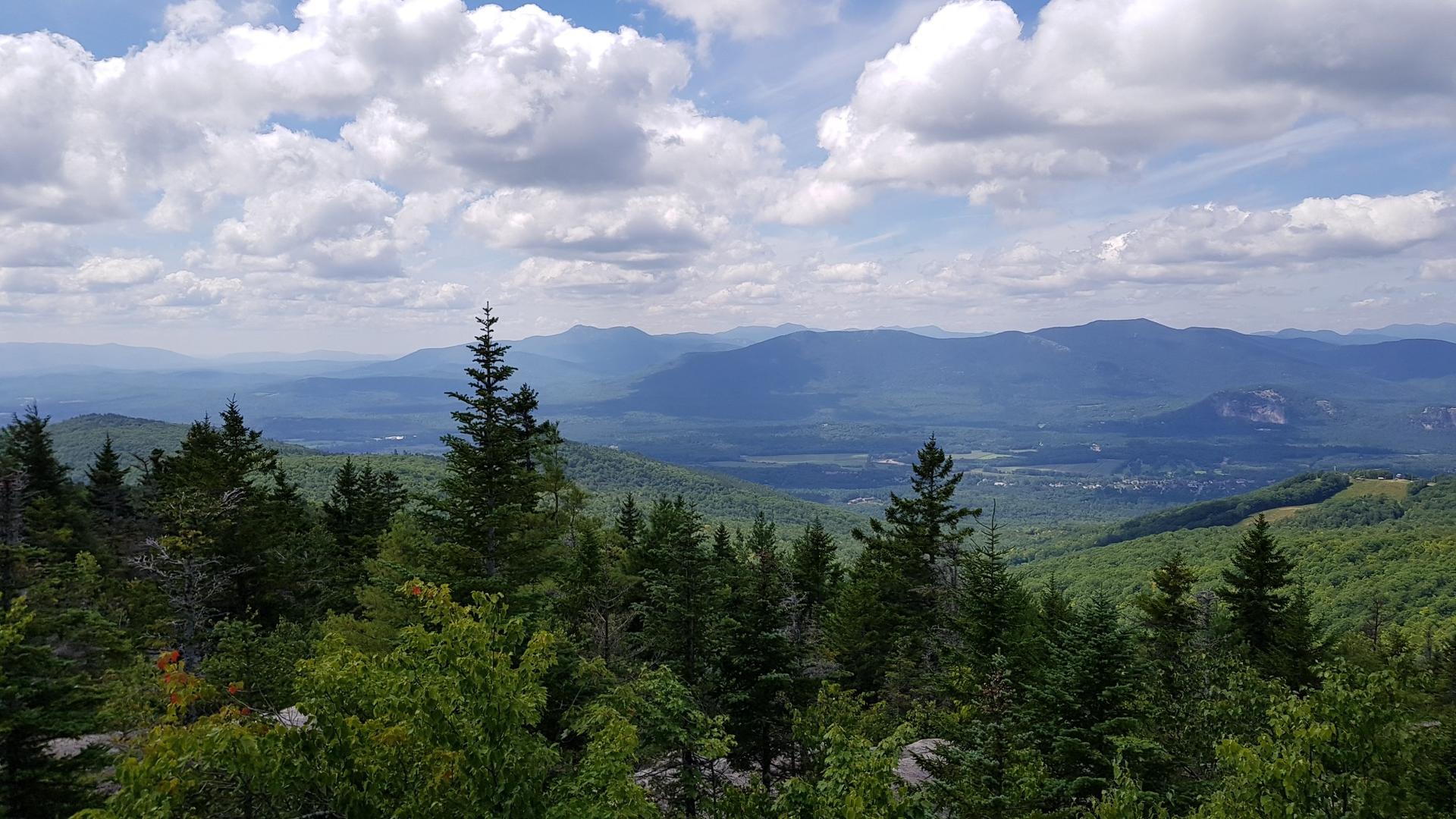 Vast mountain landscape with dense green forests under a cloudy sky.