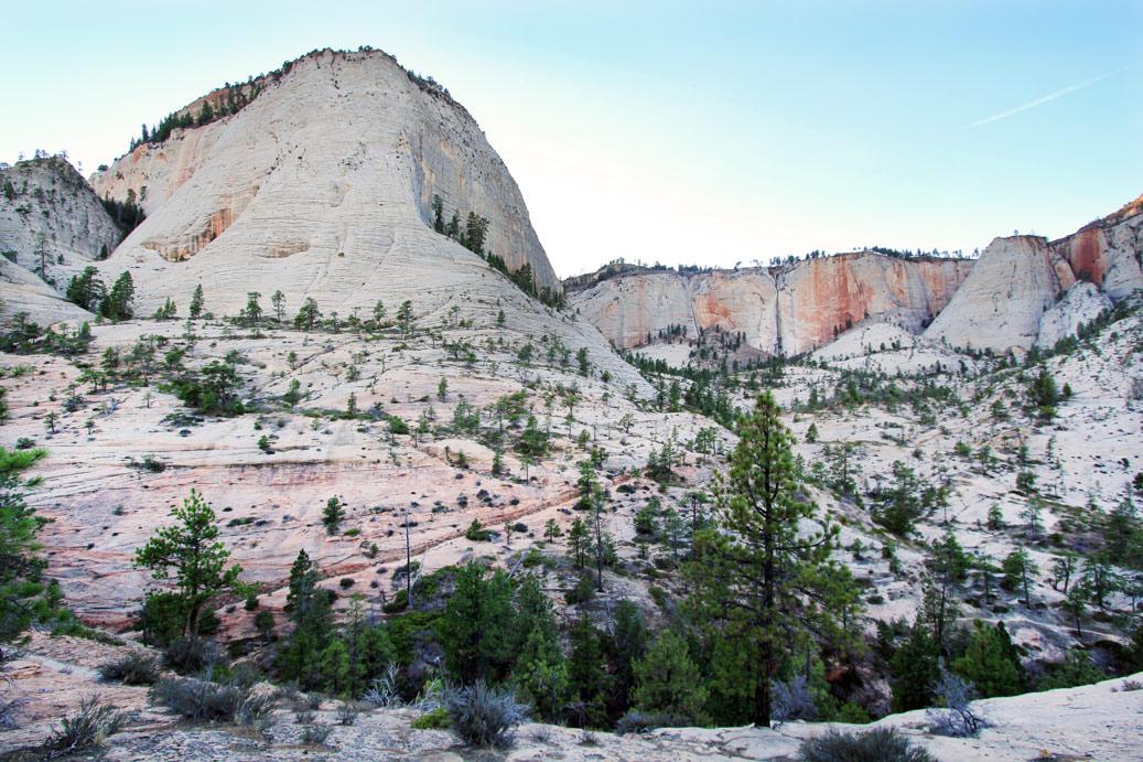 Vast light-colored mountains with sparse trees under a soft, clear sky.