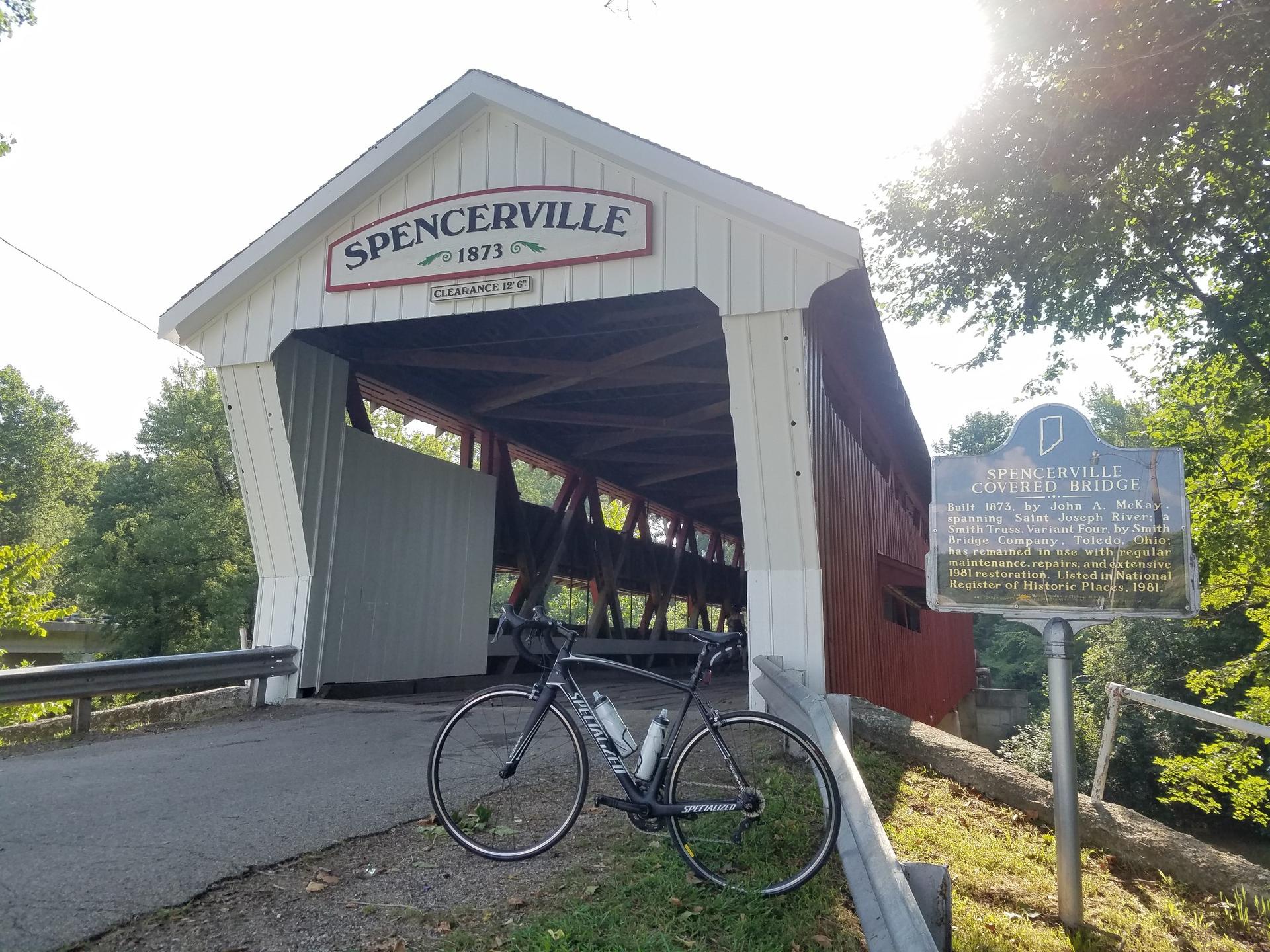 A bicycle parked beside a white and red covered bridge on a sunny day.