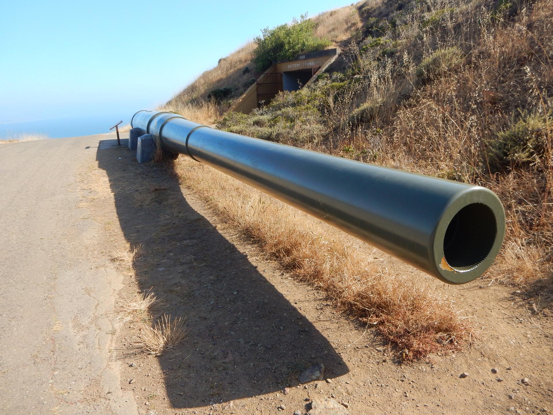 Long green pipe on a dirt path next to a dry, grassy hillside.