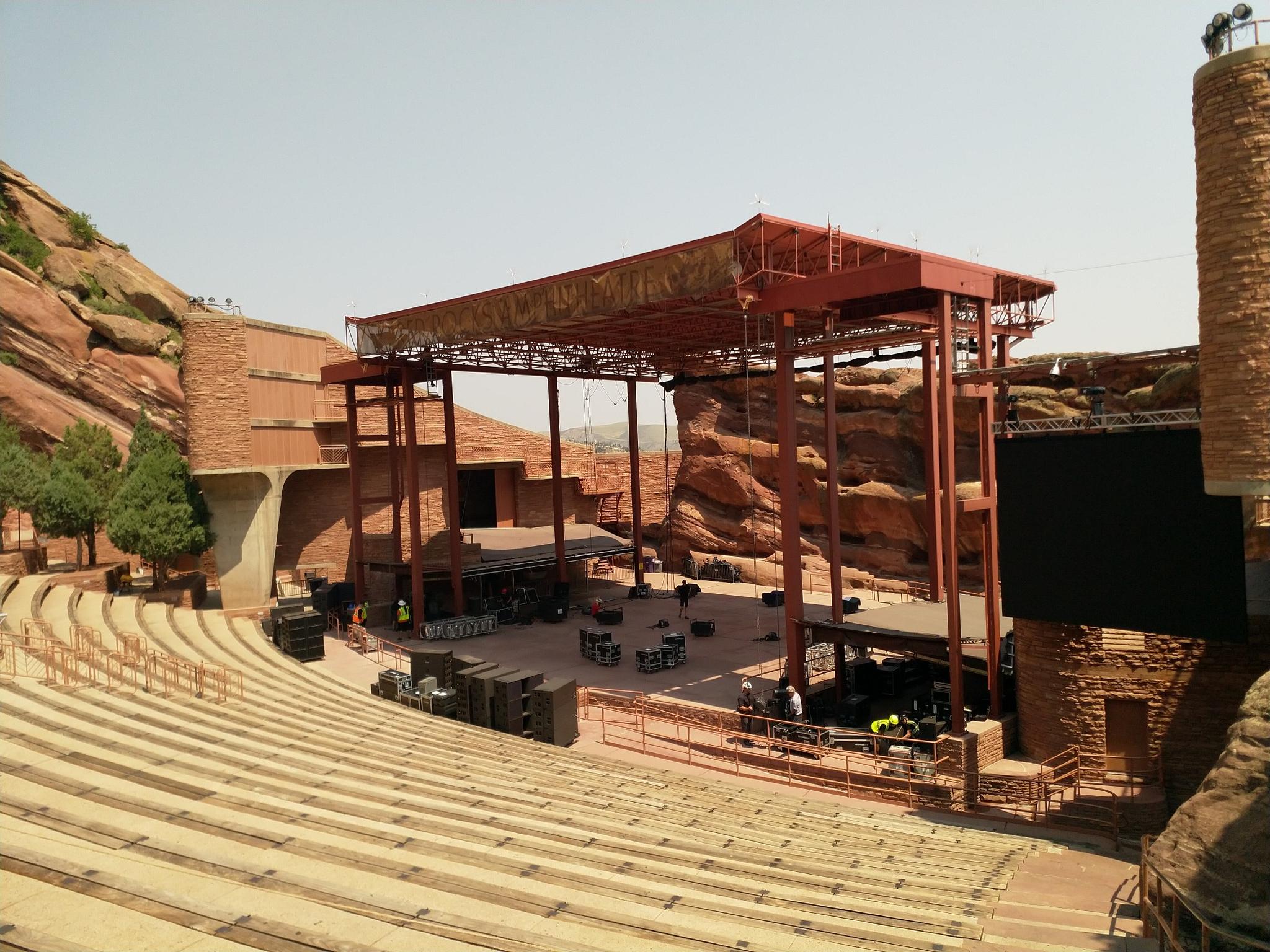 Empty outdoor amphitheater stage and tiered seating surrounded by red rocks.