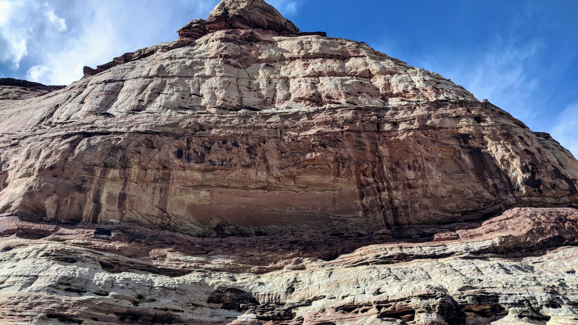 Massive, layered rock formation under a bright blue sky with clouds.