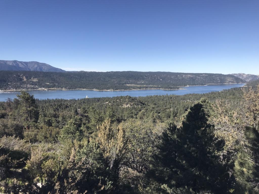 Panoramic view of a calm lake surrounded by dense forest and distant mountains.