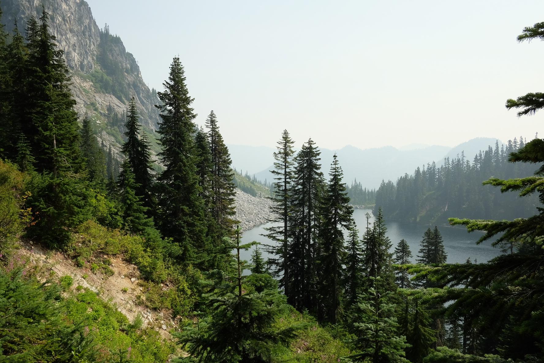 Hazy view of a lake nestled among forested mountains and rocky slopes.