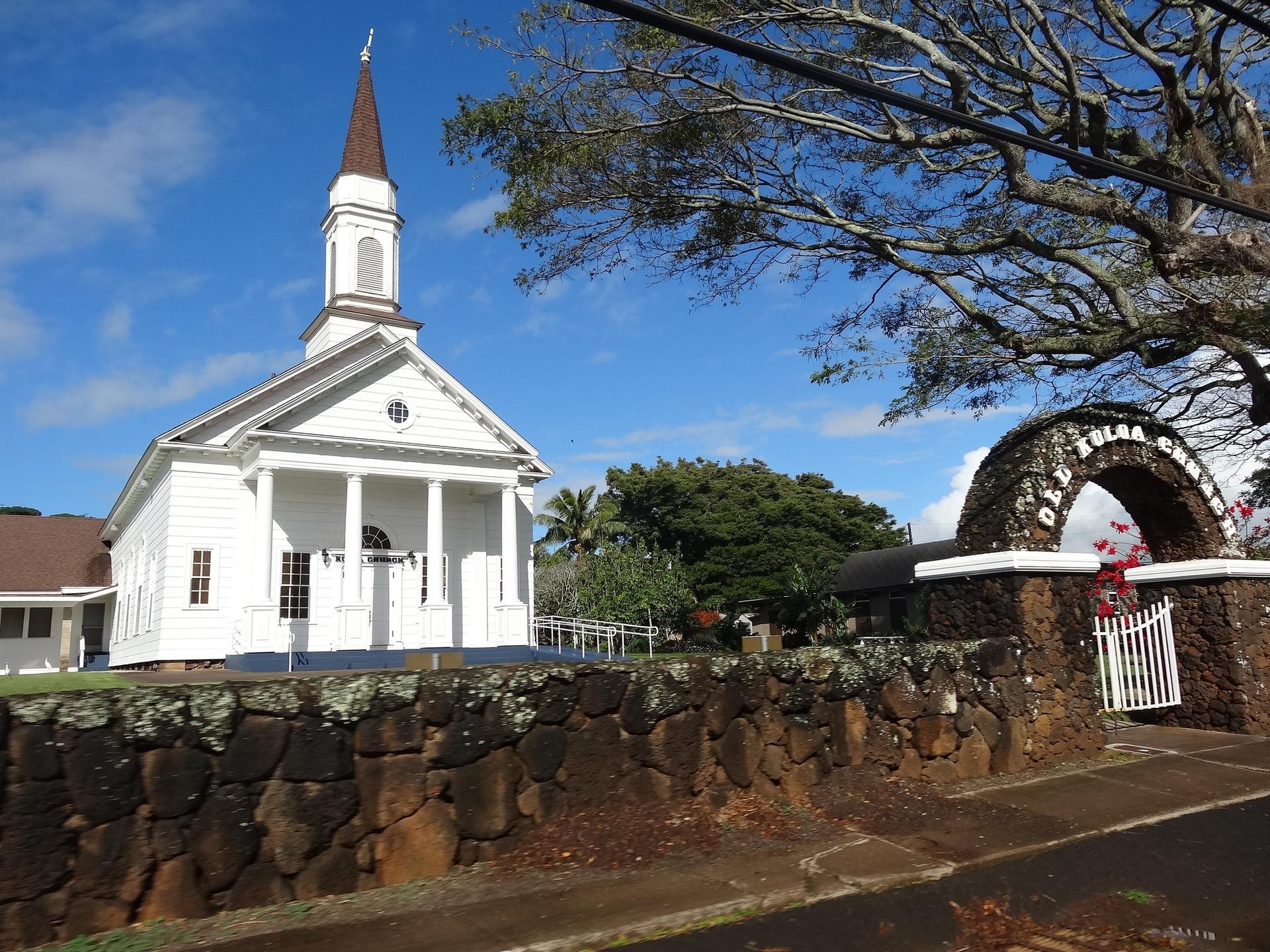 A white church with a steeple next to a stone archway under a blue sky.