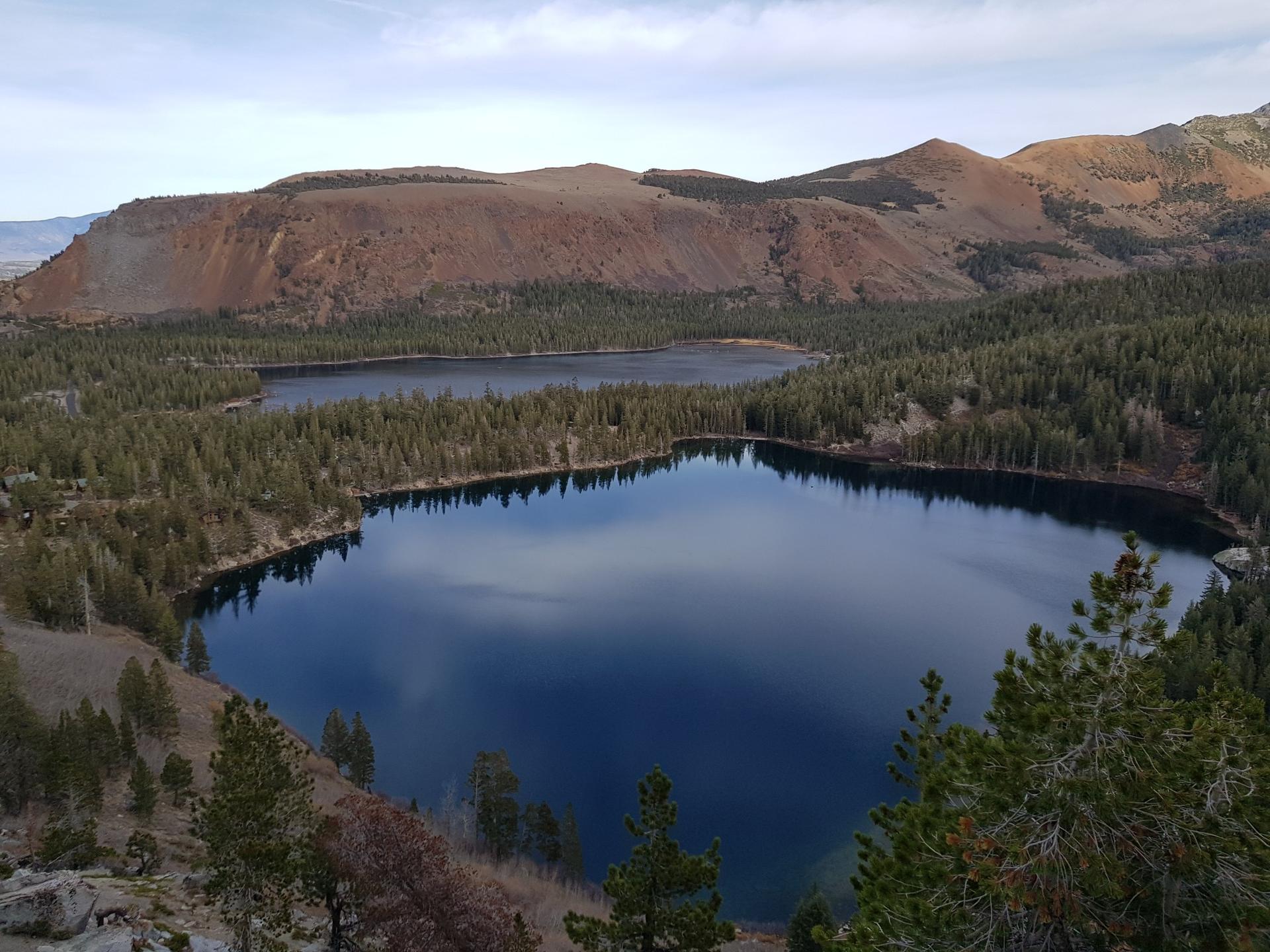 Two dark lakes surrounded by pine forests under a cloudy, muted sky.