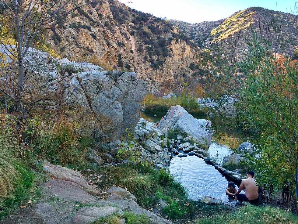 Two people by a rocky stream in a canyon, warm afternoon light.