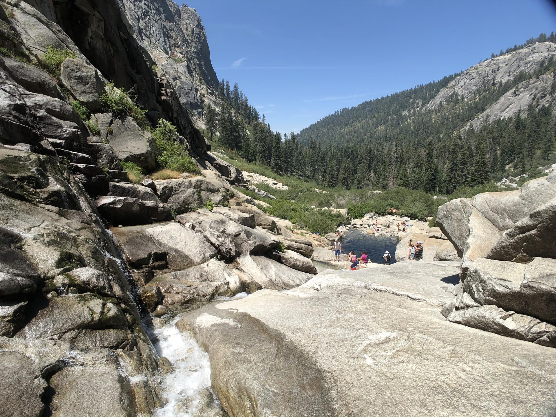People swimming in a dark pool at the base of a rocky waterfall.