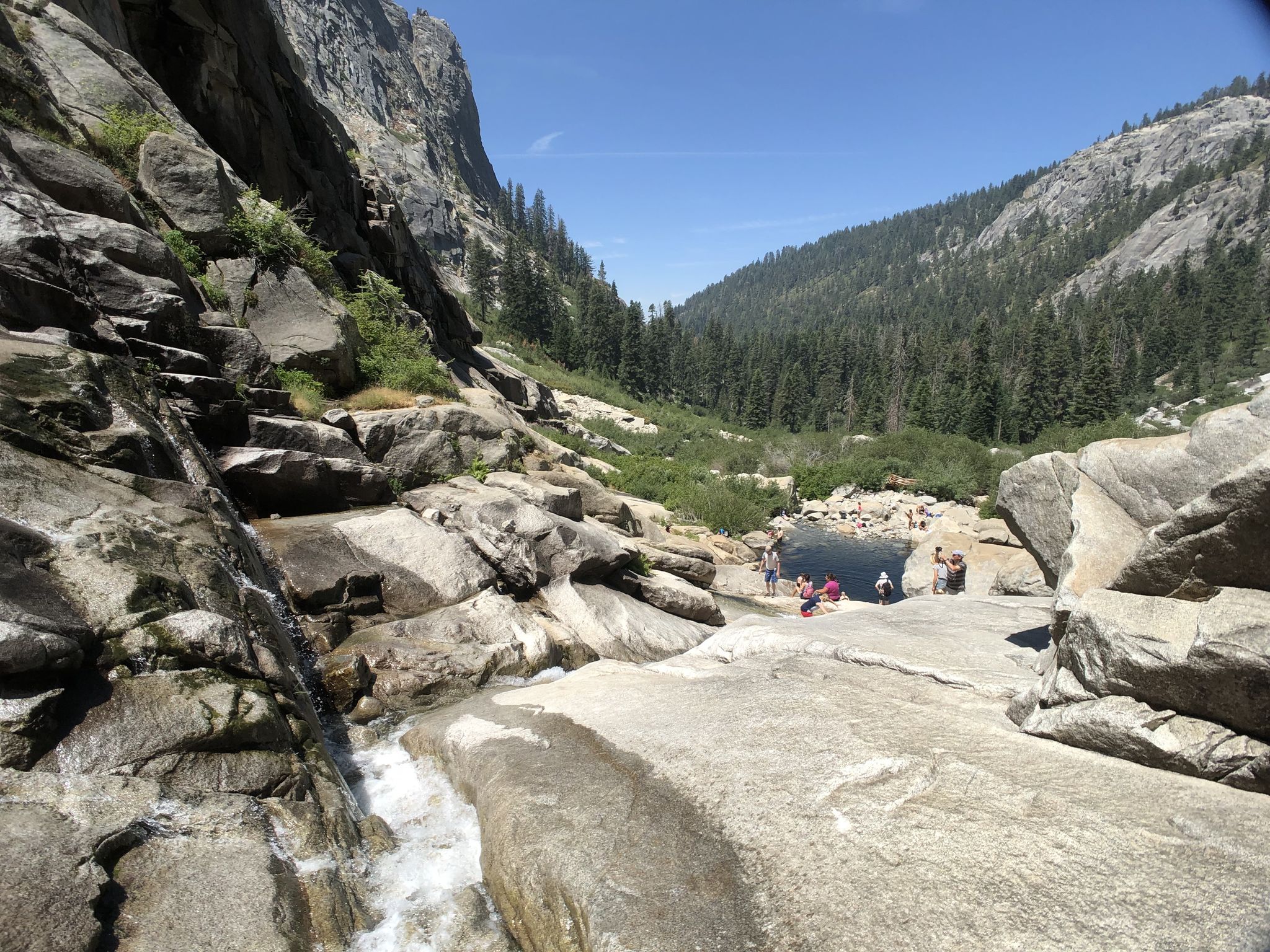 People swimming in a dark pool at the base of a rocky waterfall. - Tokopah Falls Trail