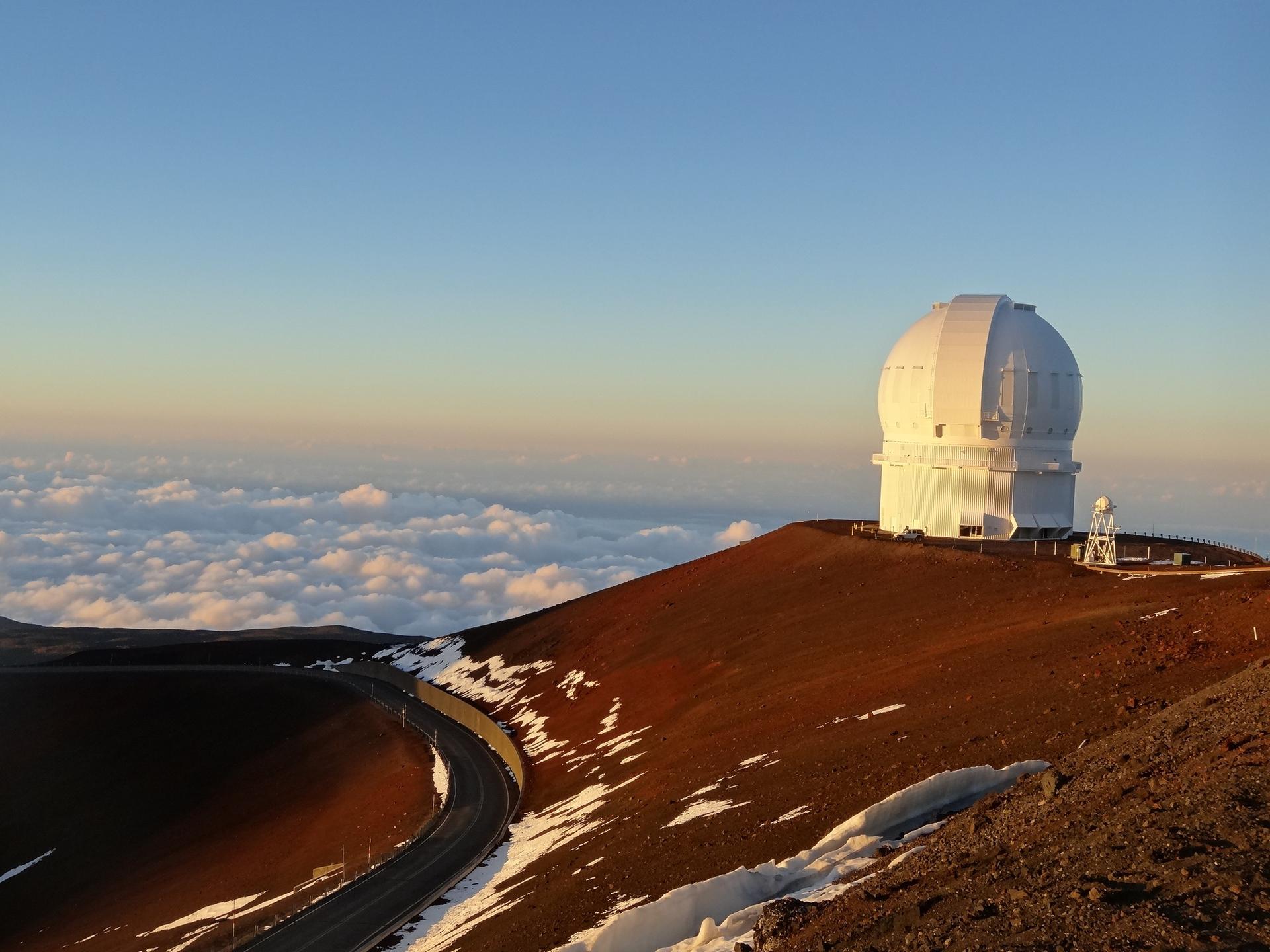 A large white observatory dome sits on a mountain peak at sunset.