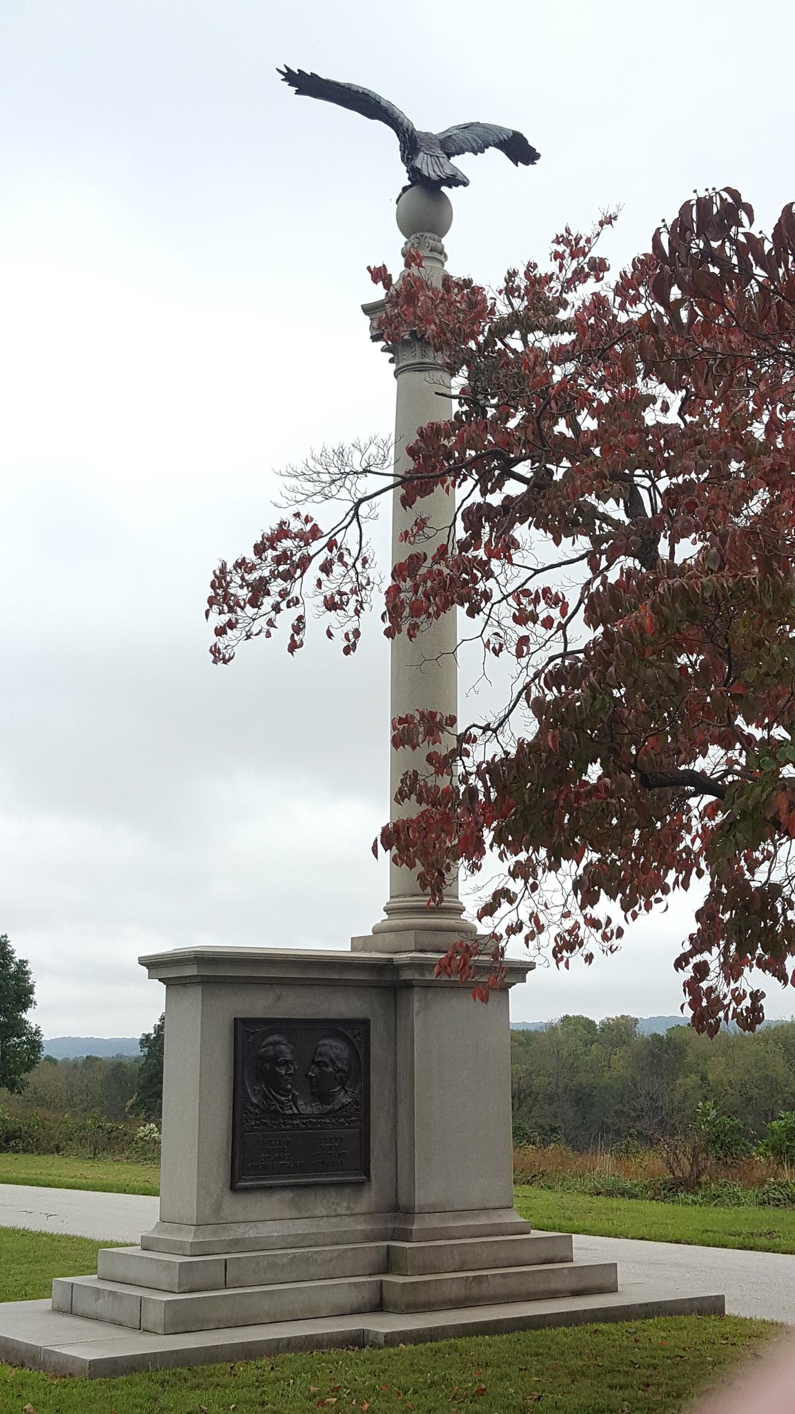 Tall monument topped with an eagle statue, next to autumn trees.