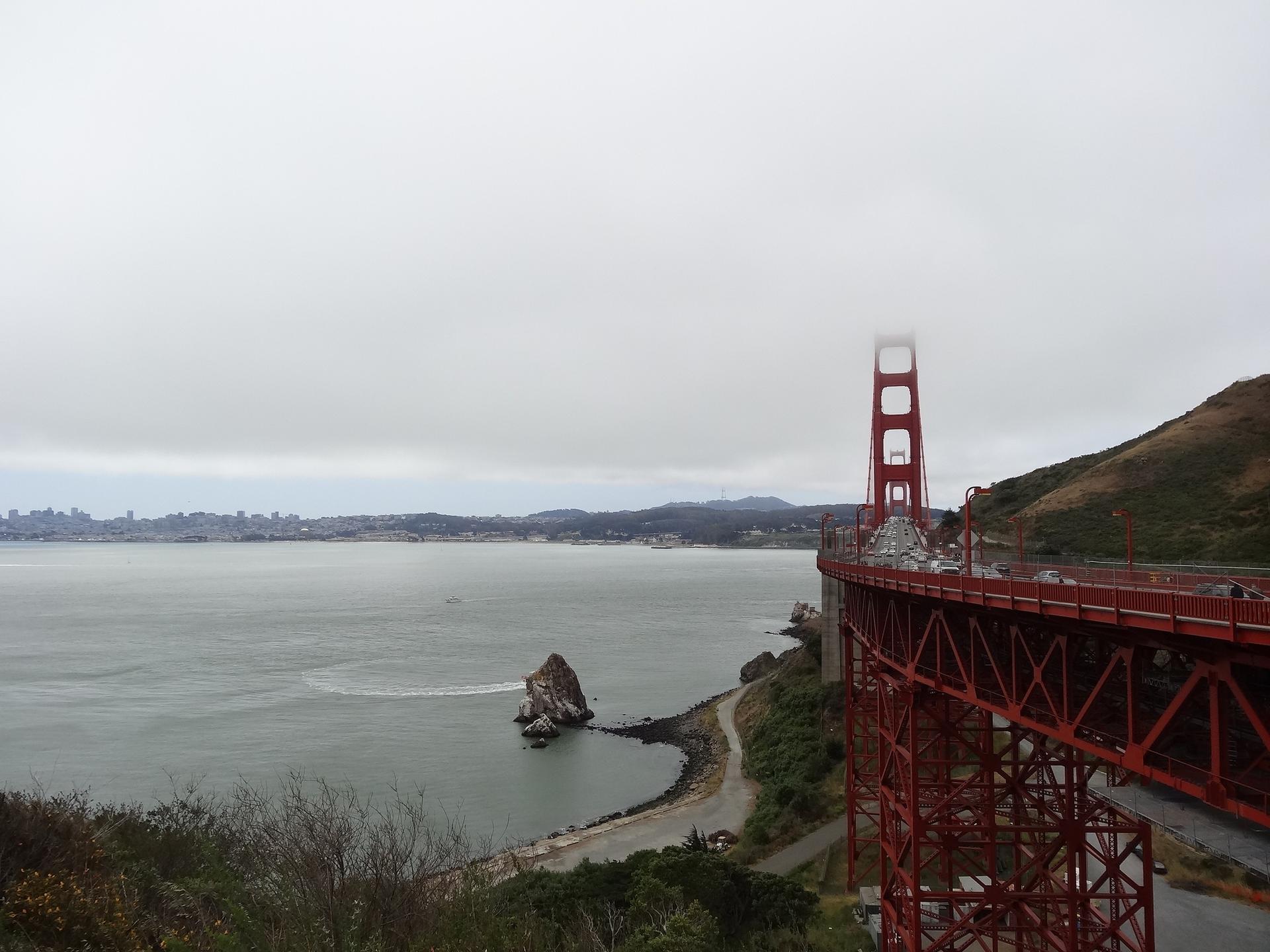 Red bridge and rocky island in a bay under an overcast sky.