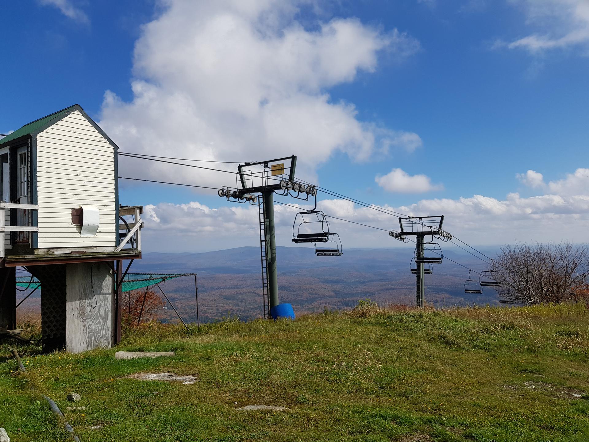 Ski lift and small building on a grassy hill overlooking distant mountains.