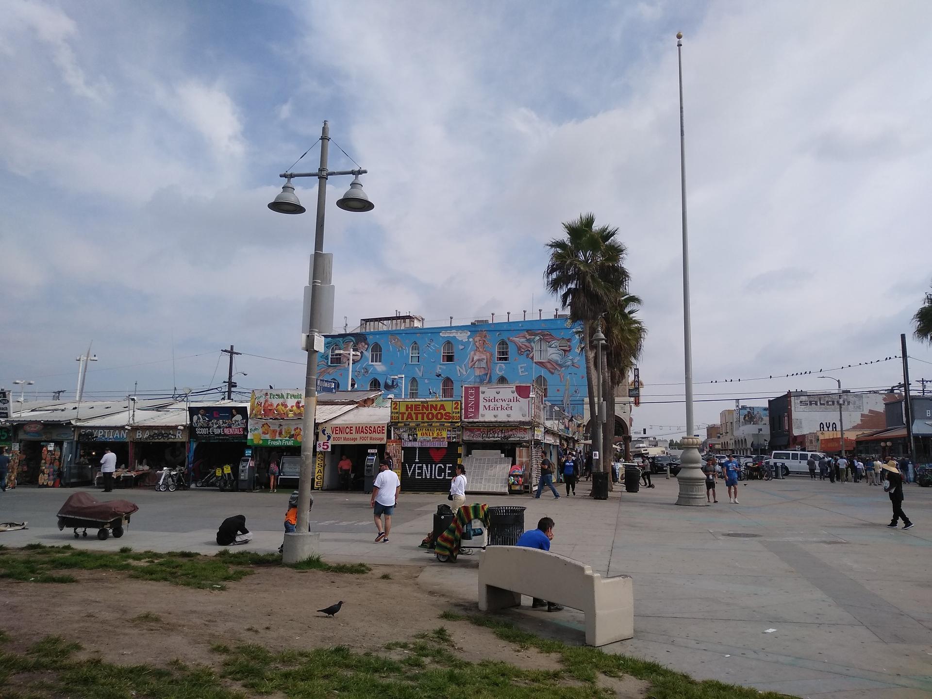 Busy street scene with colorful buildings, palm trees, and people under cloudy sky.