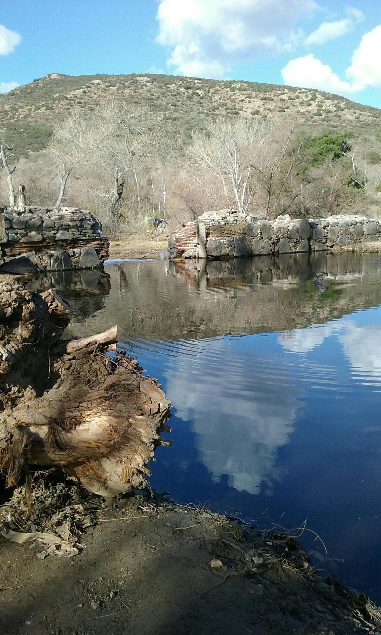 Calm water reflecting blue sky, surrounded by rocks and bare trees.