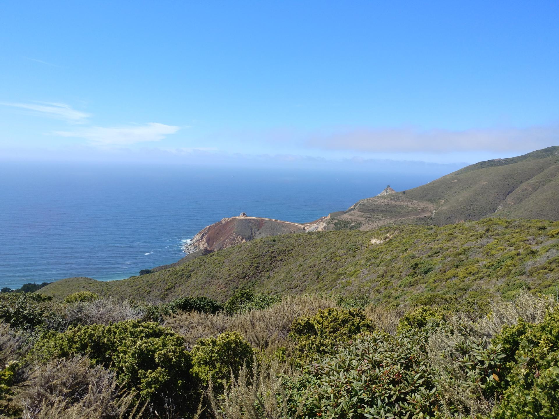 A panoramic view of a vast blue ocean next to green, rugged hills.