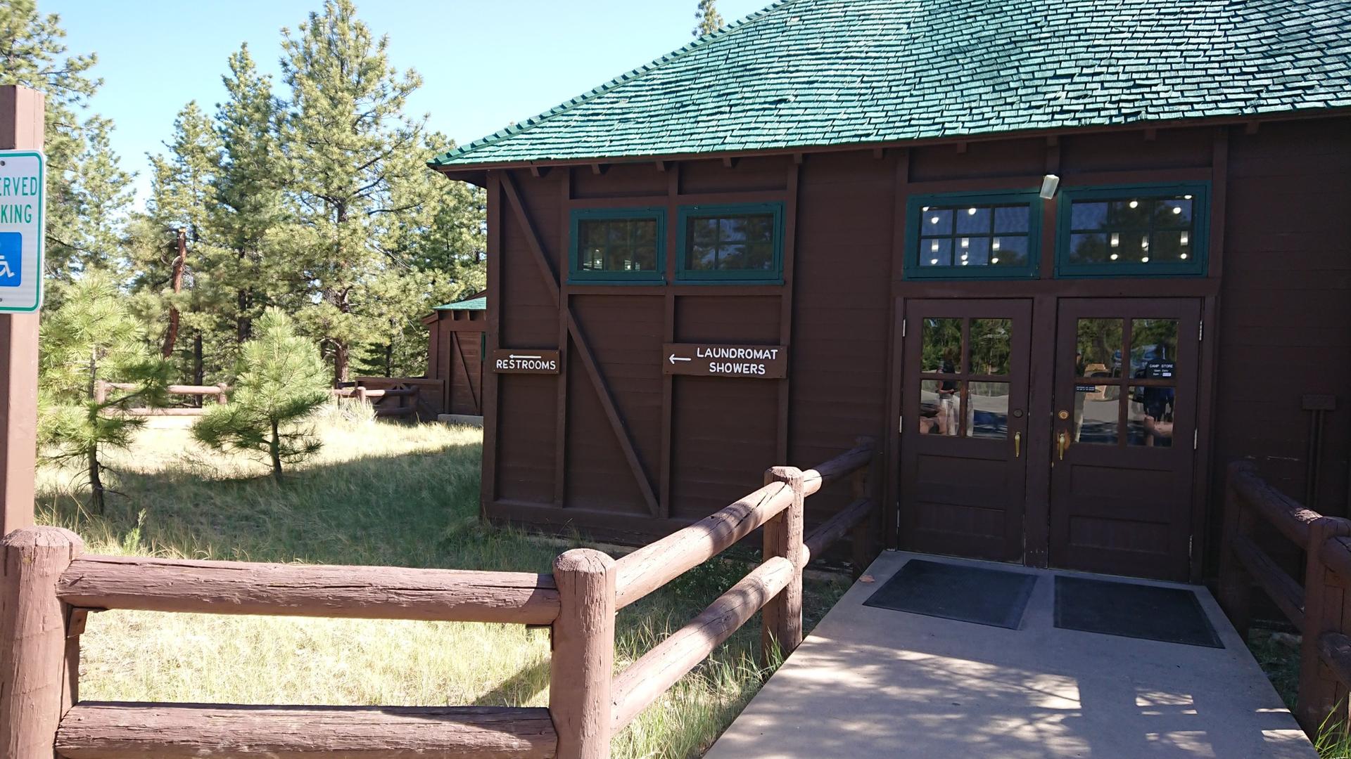 Brown building with green roof, signs for restrooms and laundromat, wooden fence.