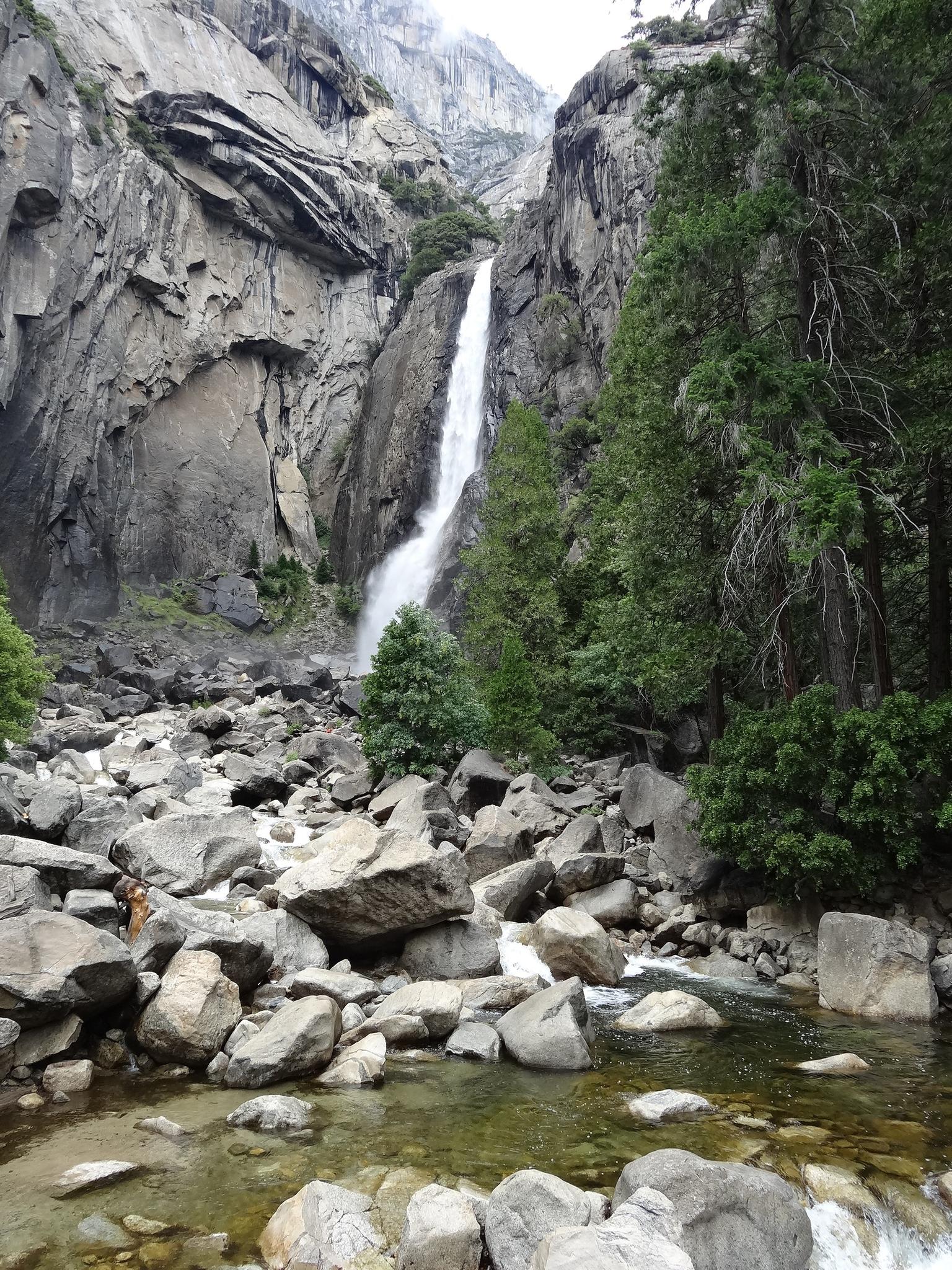 Powerful waterfall plunging into a rocky riverbed, surrounded by cliffs and trees.