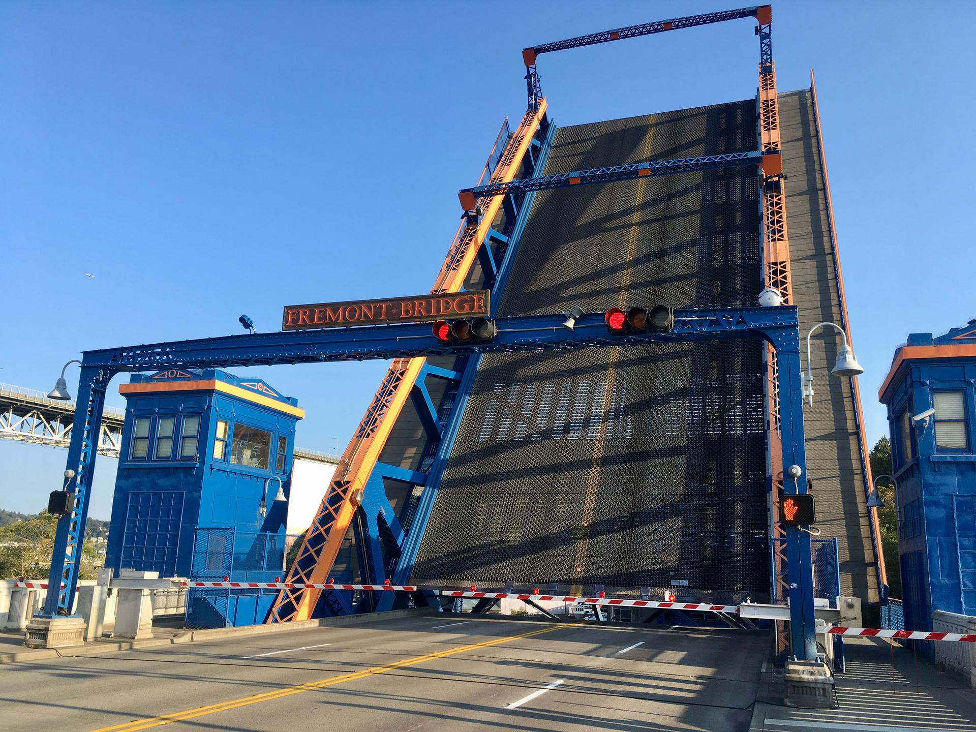 A large blue drawbridge is open, angled upwards, under a clear sky.