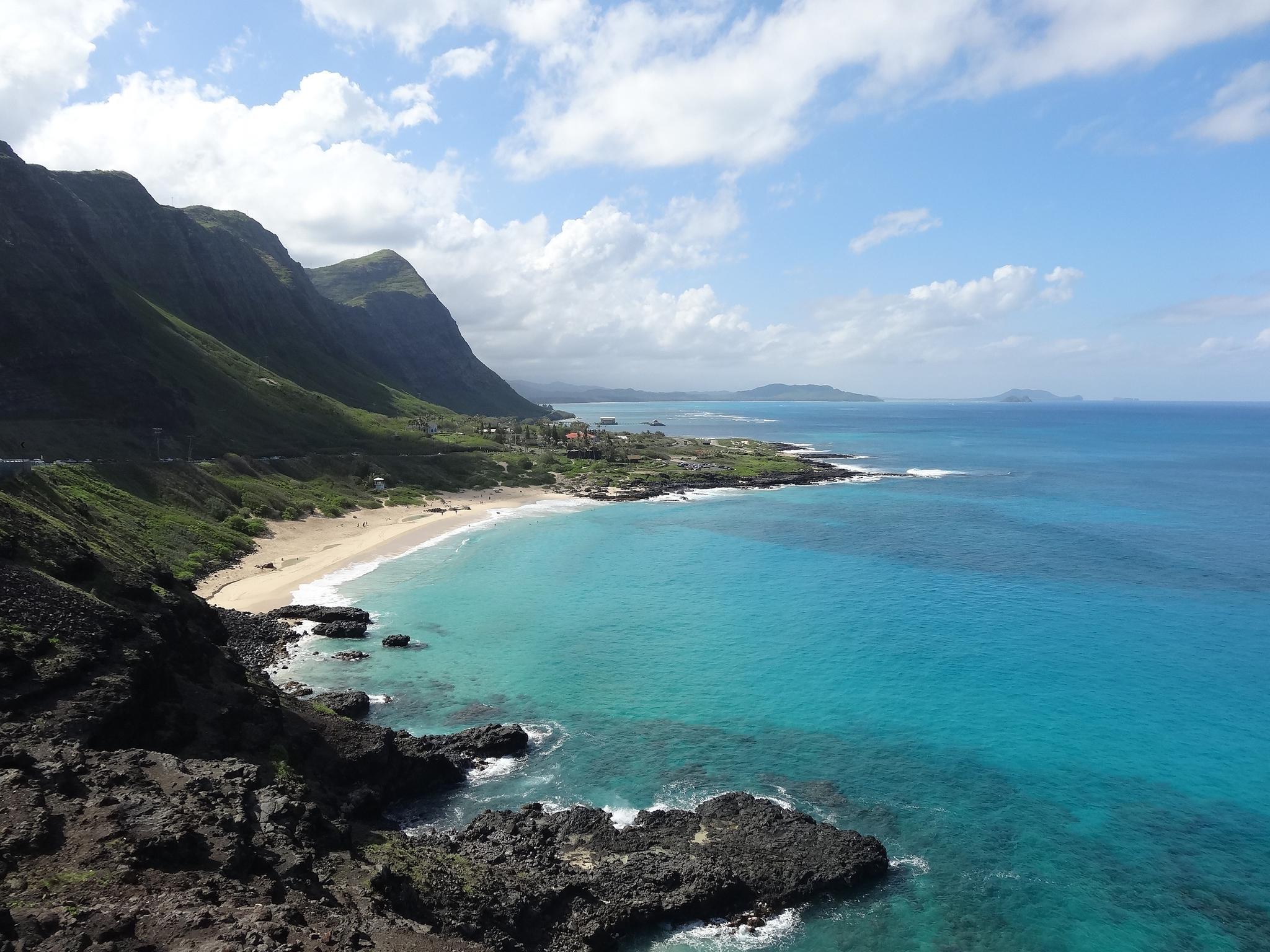 Turquoise ocean, sandy beach, and green mountains under a blue sky.