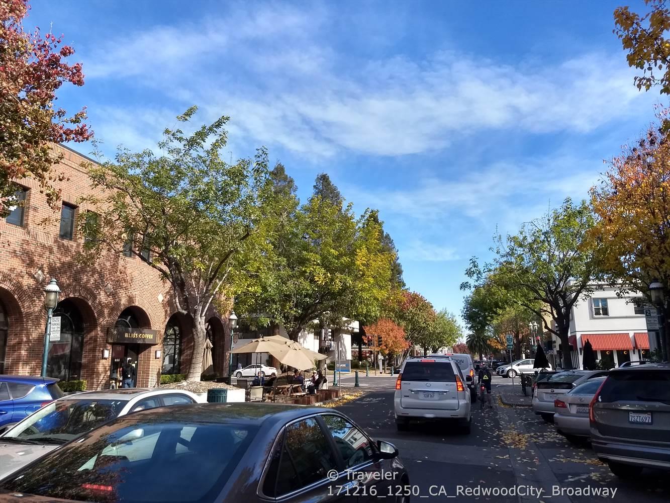 Busy city street with cars, brick buildings, and trees with autumn leaves.