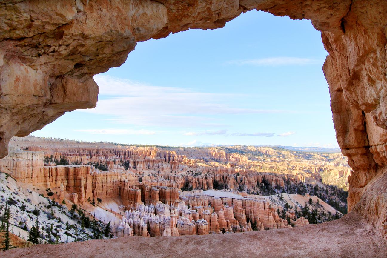 Wide view of sunlit red rock hoodoos through a natural rock arch.