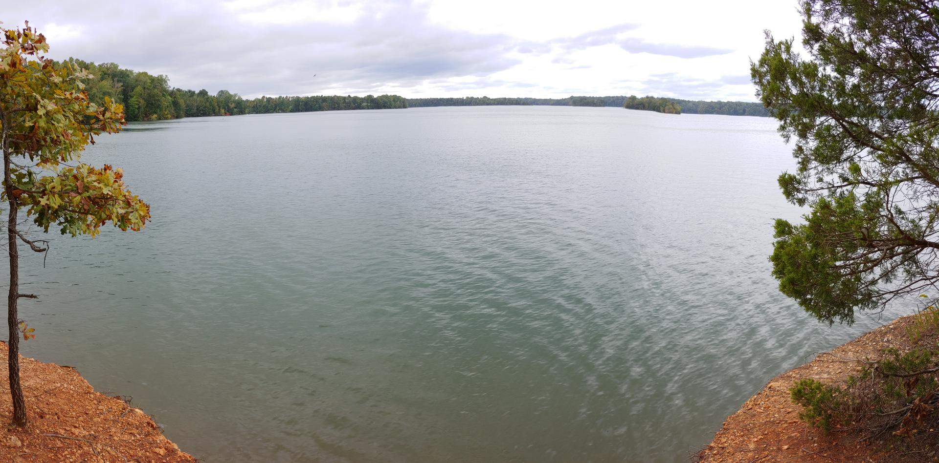 An expansive lake with a distant tree-lined shore under a cloudy sky.