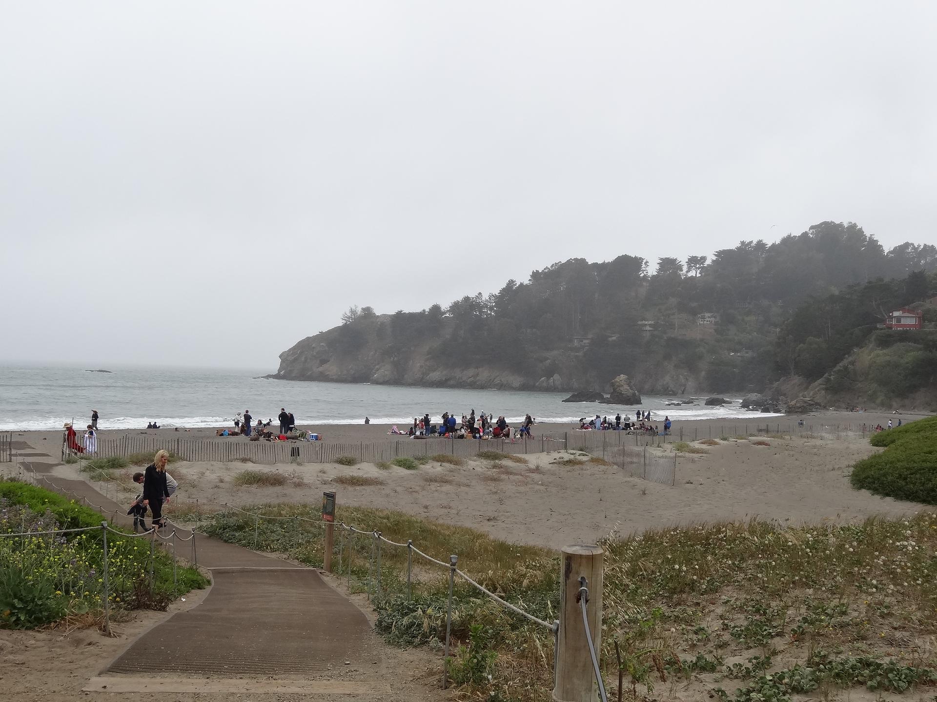 Many people on a misty beach with cliffs and ocean waves.
