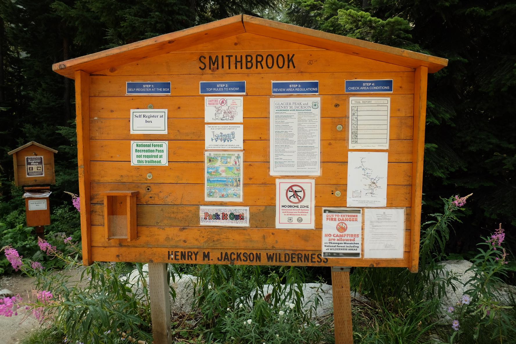 A large wooden information board with various notices in a green setting.