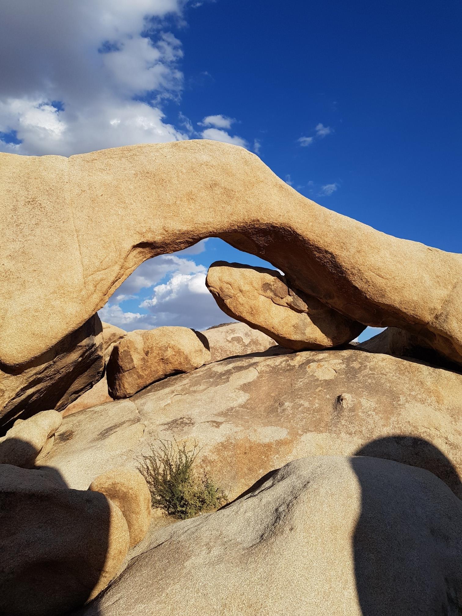 Natural rock arch against a bright blue sky with white clouds.