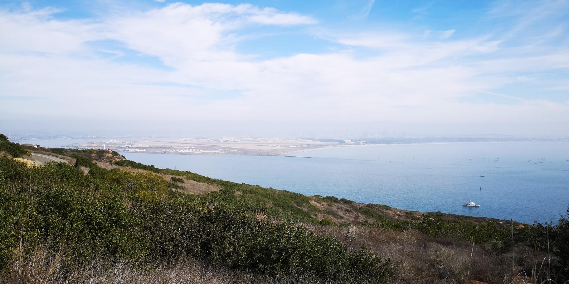 Hazy panoramic view of a bay and distant city from a green hillside.