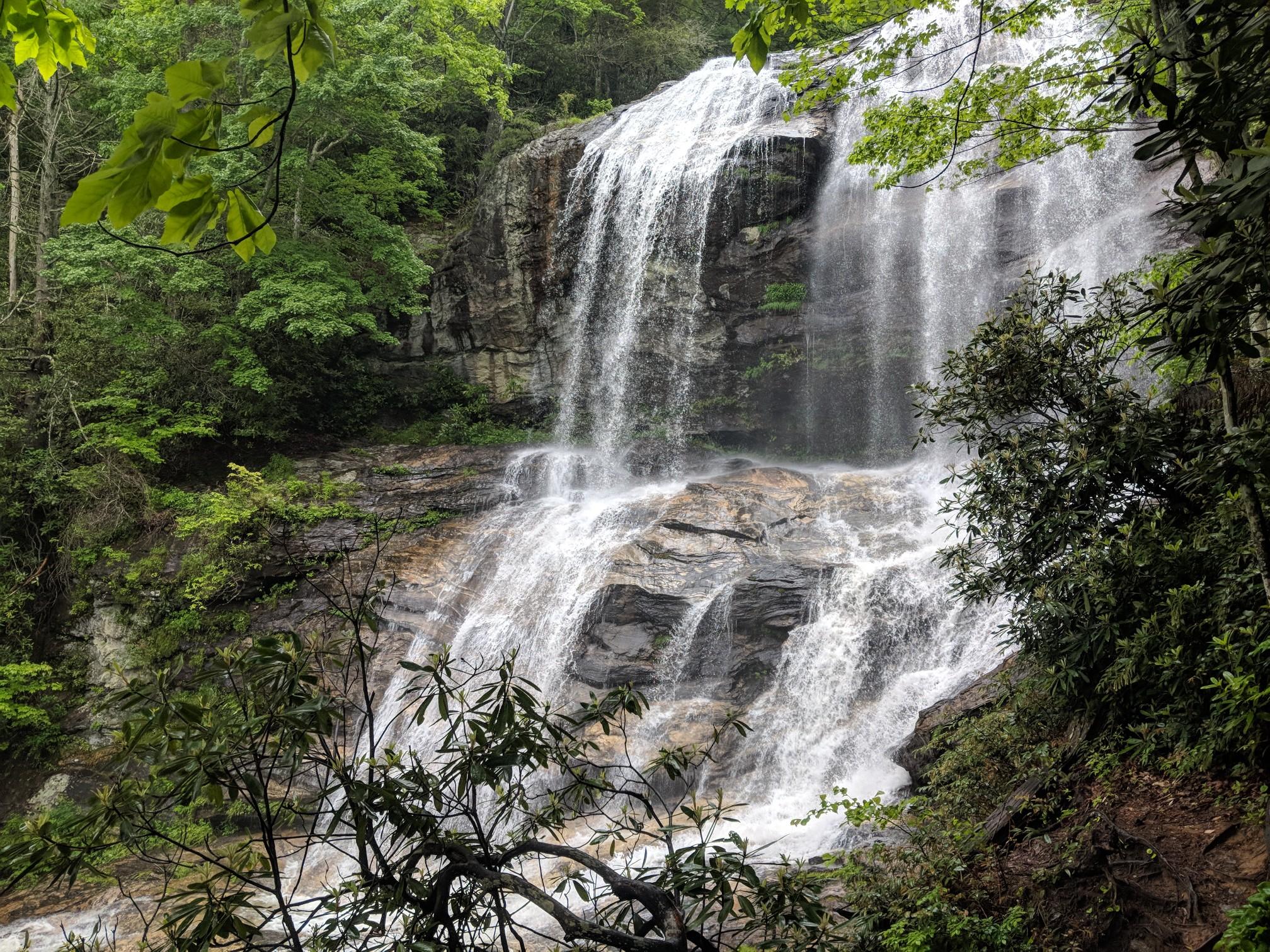 Tall, multi-tiered waterfall cascades down dark rocks in a green forest.
