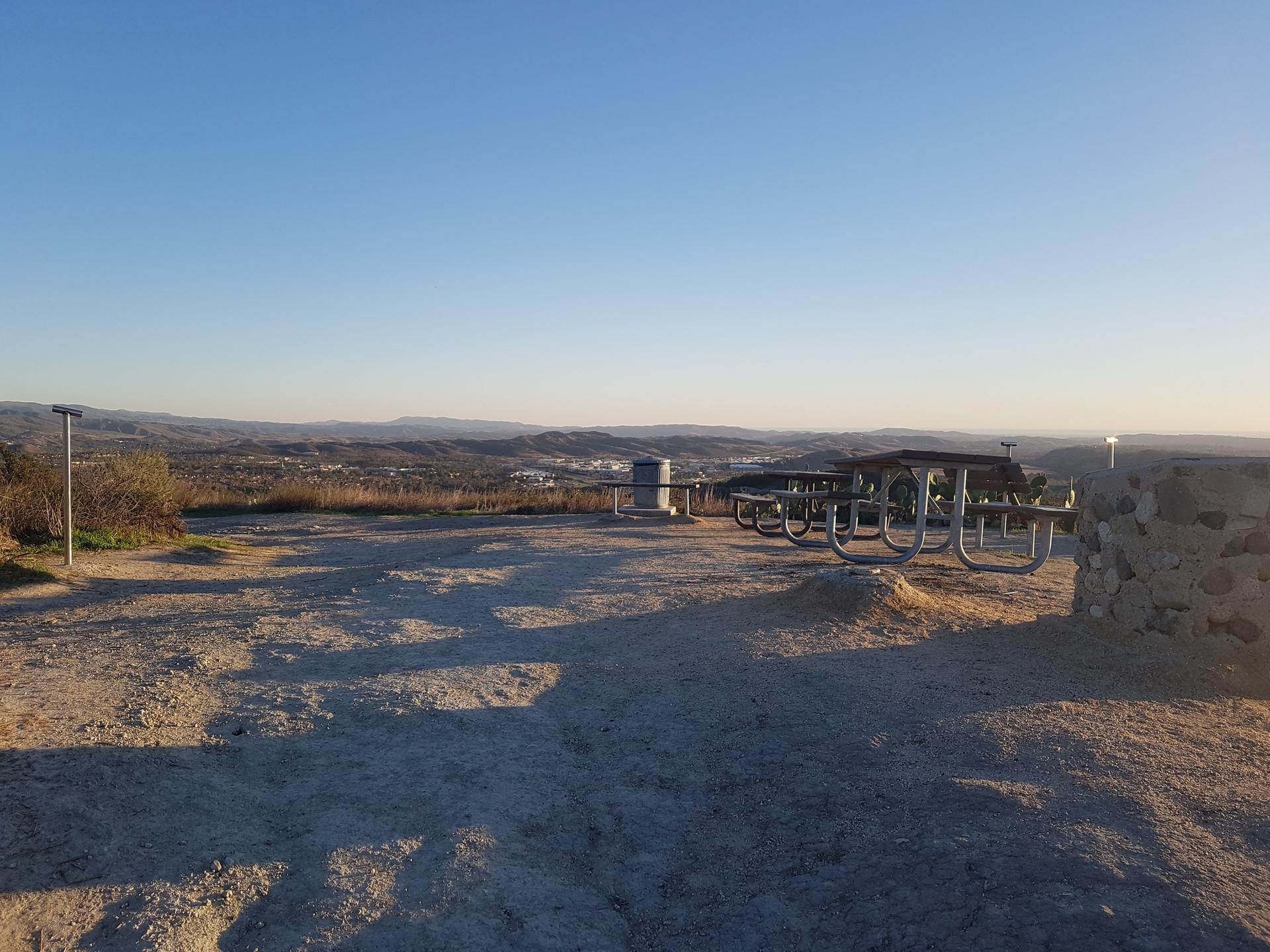 Picnic tables on a hilltop overlooking a valley under a clear sky.
